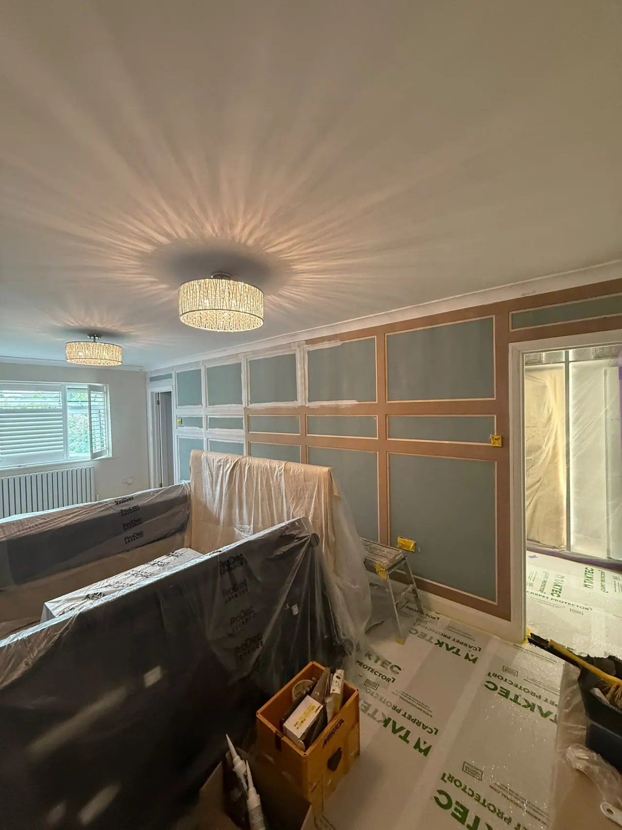 Room during painting and decorating preparation, furniture protected and panelling being fitted