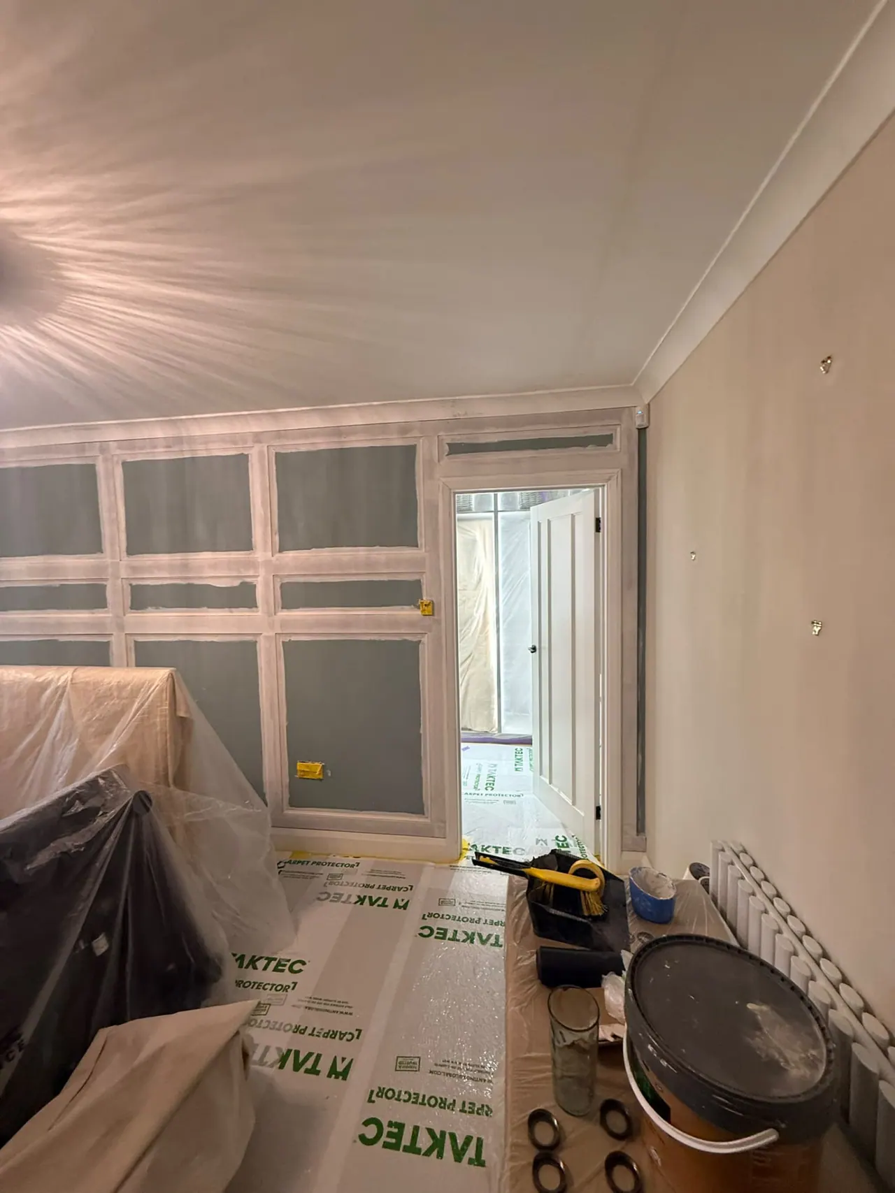 Room during painting and decorating preparation, furniture protected and panelling being fitted